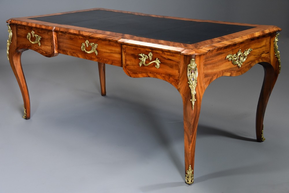 A mid-19th-century French-style writing desk made from figured Goncalo Alves timber, featuring three drawers, gilt bronze Rococo mounts, cabriole legs, and a black leather inset top. View II