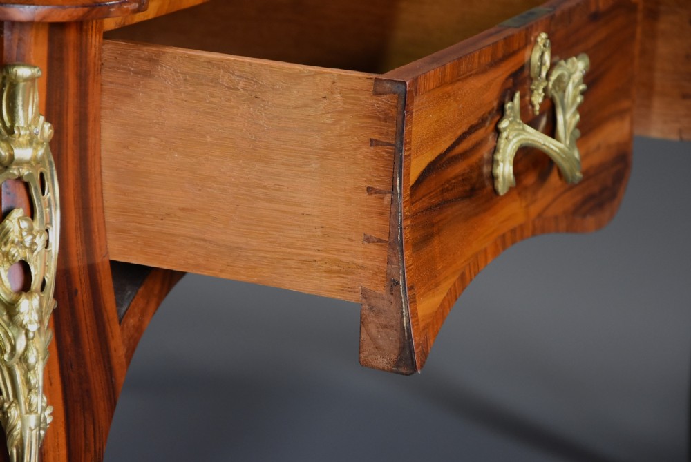 A mid-19th-century French-style writing desk made from figured Goncalo Alves timber, featuring three drawers, gilt bronze Rococo mounts, cabriole legs, and a black leather inset top. View V
