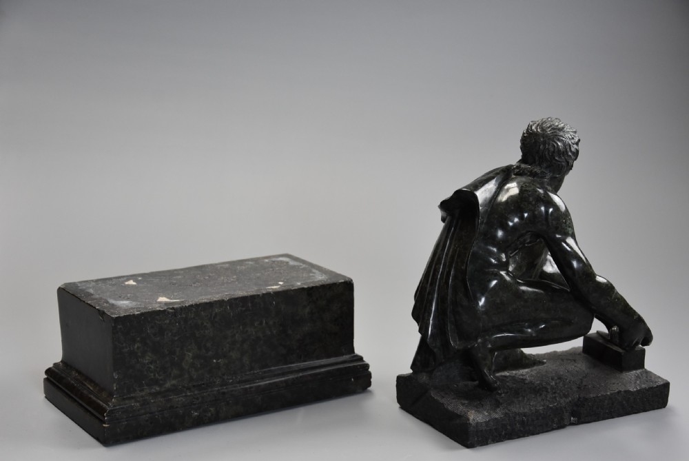 A dark green carved marble sculpture of the classical crouching figure Arrotino mounted on a rectangular plinth. View X