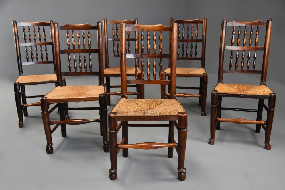 A set of six early nineteenth-century ash and elm spindle back dining chairs featuring woven rush seats and turned wooden stretchers.