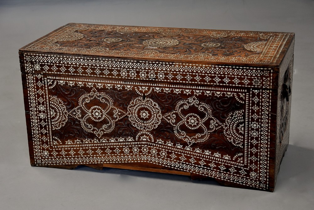 A dark hardwood rectangular storage trunk decorated with detailed relief carving and intricate geometric mother of pearl inlay across the front panel and lid. View II