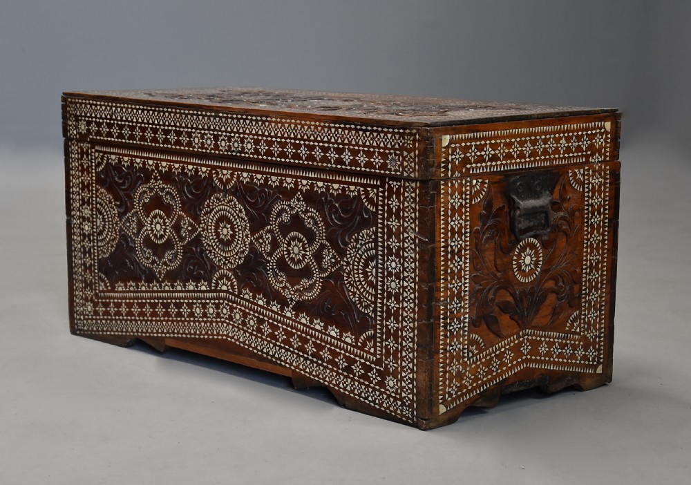 A dark hardwood rectangular storage trunk decorated with detailed relief carving and intricate geometric mother of pearl inlay across the front panel and lid. View III