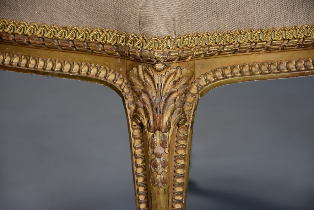 A mid-19th-century French carved giltwood footstool with a padded neutral linen seat, floral carving, and sweeping cabriole legs ending in scroll feet. View VII