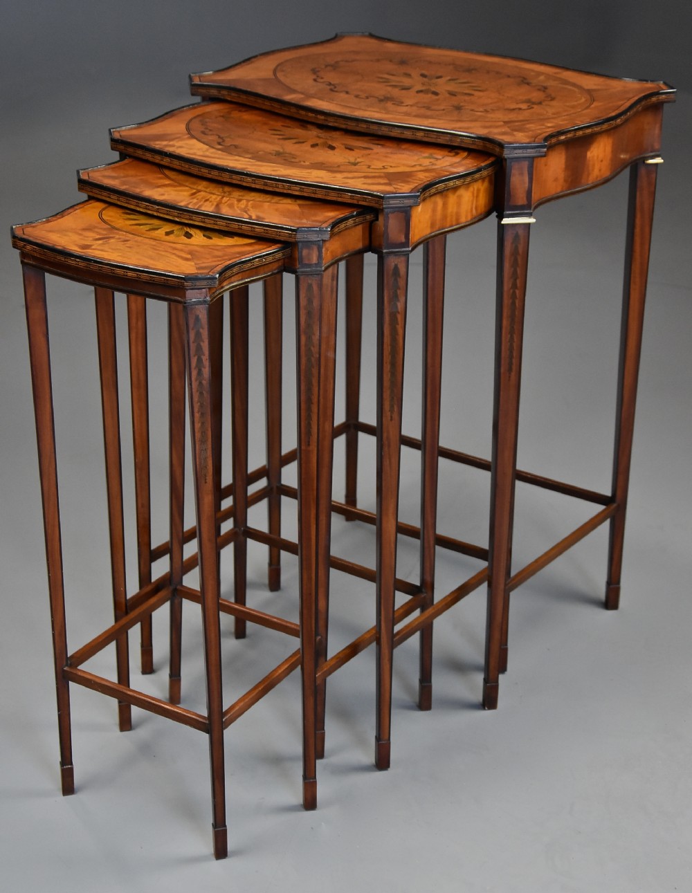 A set of four graduated Edwardian style satinwood nesting tables with serpentine tops, floral marquetry inlays, and slender tapered legs.