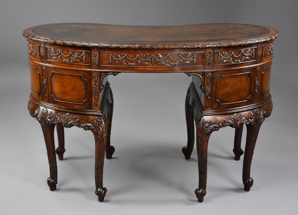 An Edwardian kidney-shaped mahogany desk featuring an inlaid leather top, relief carvings on drawer fronts, cabriole legs, and brass handles. View XI