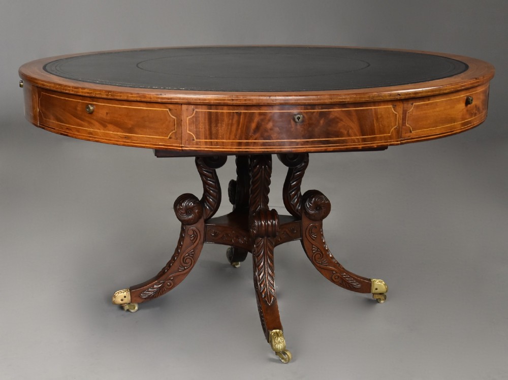 An early nineteenth-century circular mahogany drum table featuring a black leather inset top, frieze drawers, and carved scroll legs with brass castors.