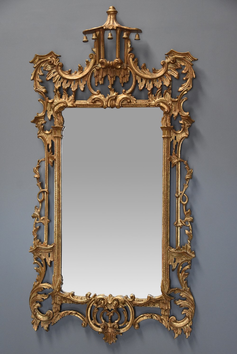 An ornate carved giltwood wall mirror in the Chinese Chippendale style featuring a pagoda pediment with hanging bells and asymmetric Rococo foliage framing a rectangular mirror plate.