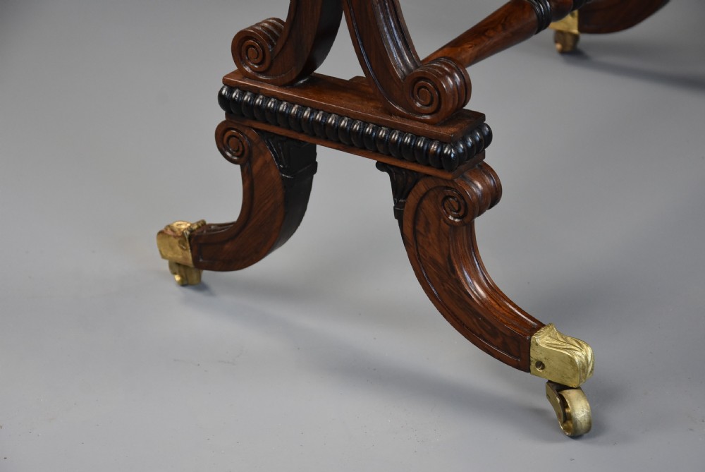 An early nineteenth-century rosewood occasional table featuring a rectangular top with a single drawer, scrolled trestle supports, beaded mouldings, and brass castors. View XIV