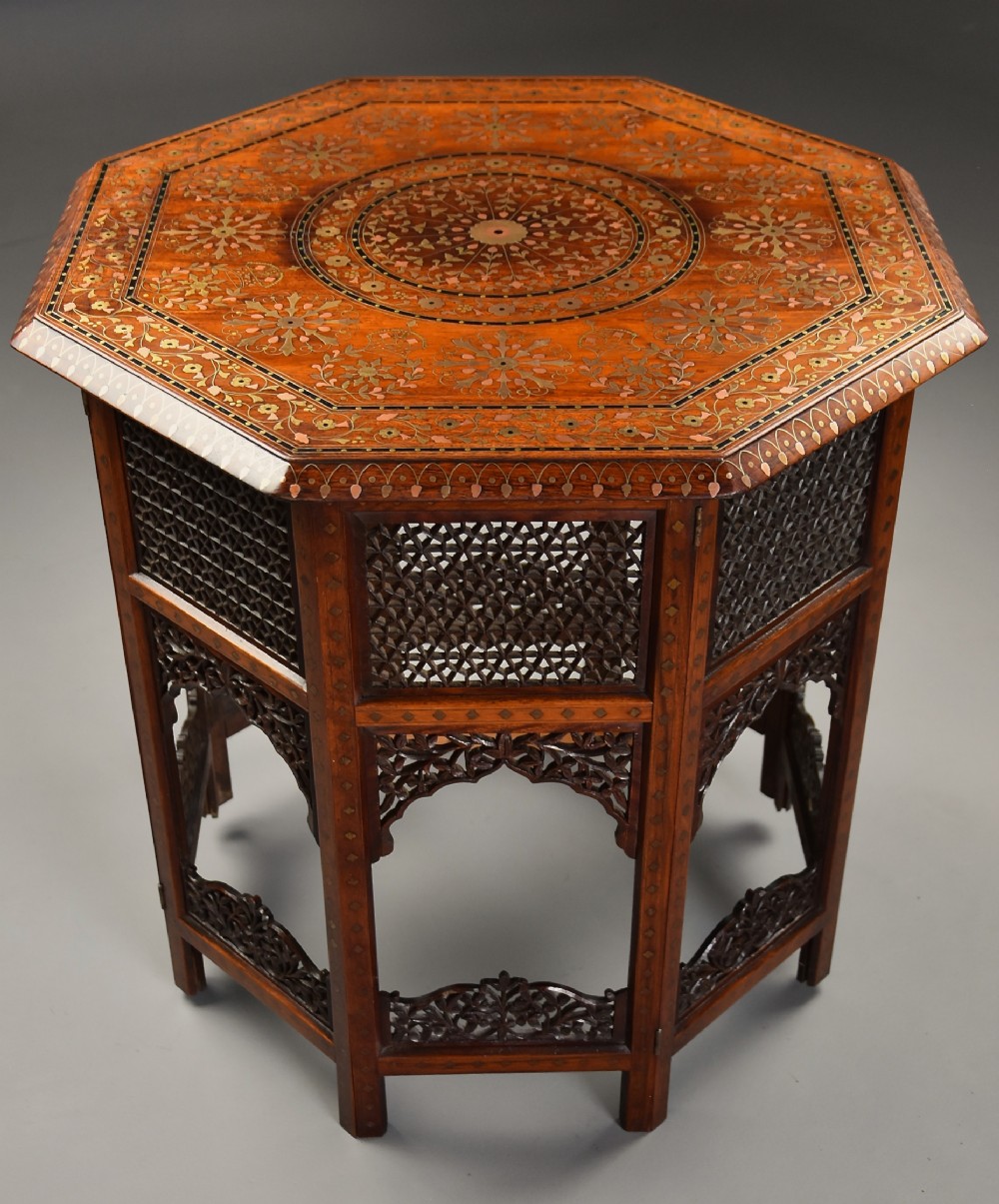 A late nineteenth-century Anglo-Indian octagonal table crafted from dark wood with intricate floral bone inlay on top and carved fretwork panels along the base.