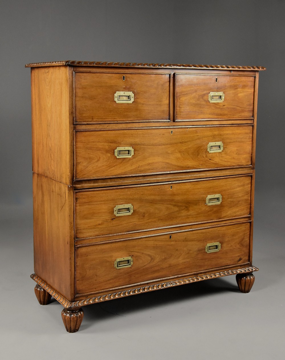 A late nineteenth-century padouk military chest of drawers featuring flush brass handles, carved rope-twist borders, and short fluted legs.