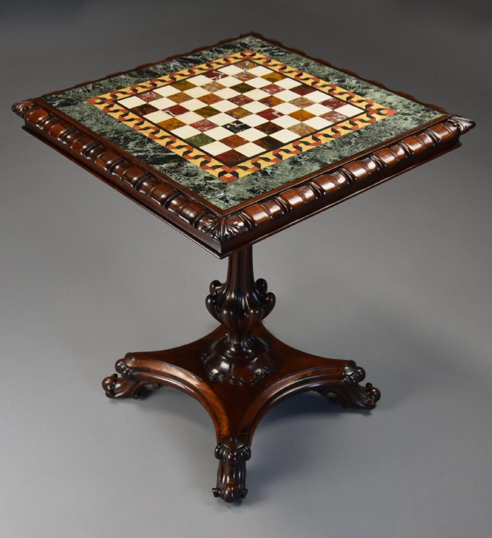 A mid-19th century rosewood games table featuring a square specimen marble inlaid chessboard top resting on a carved pedestal stem and scroll feet.