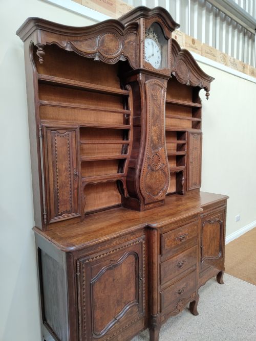 fig 1. A carved oak French provincial clock dresser featuring an integrated central longcase clock, open shelving, and a lower sideboard with drawers and cupboards.