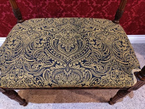 fig 1. An antique carved wooden piano stool featuring raised side handles and a gold and black patterned upholstered cushion.