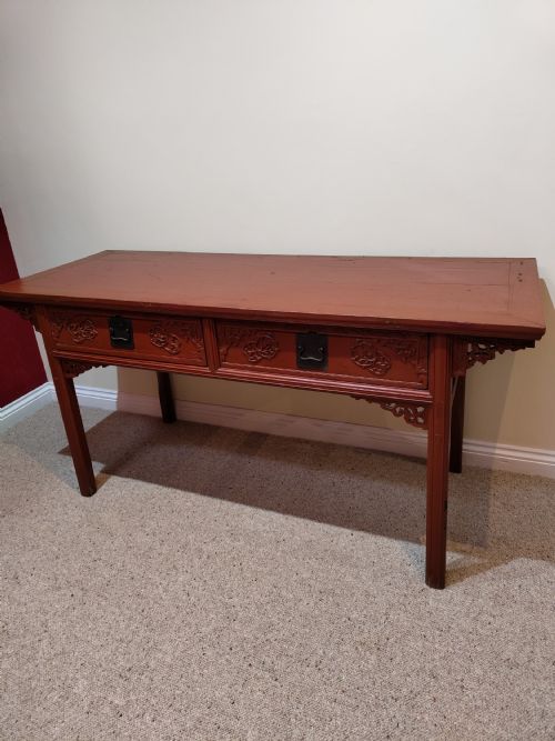fig 1. An antique Chinese red lacquer console table featuring two carved drawers with dark metal handles and extended top edges.