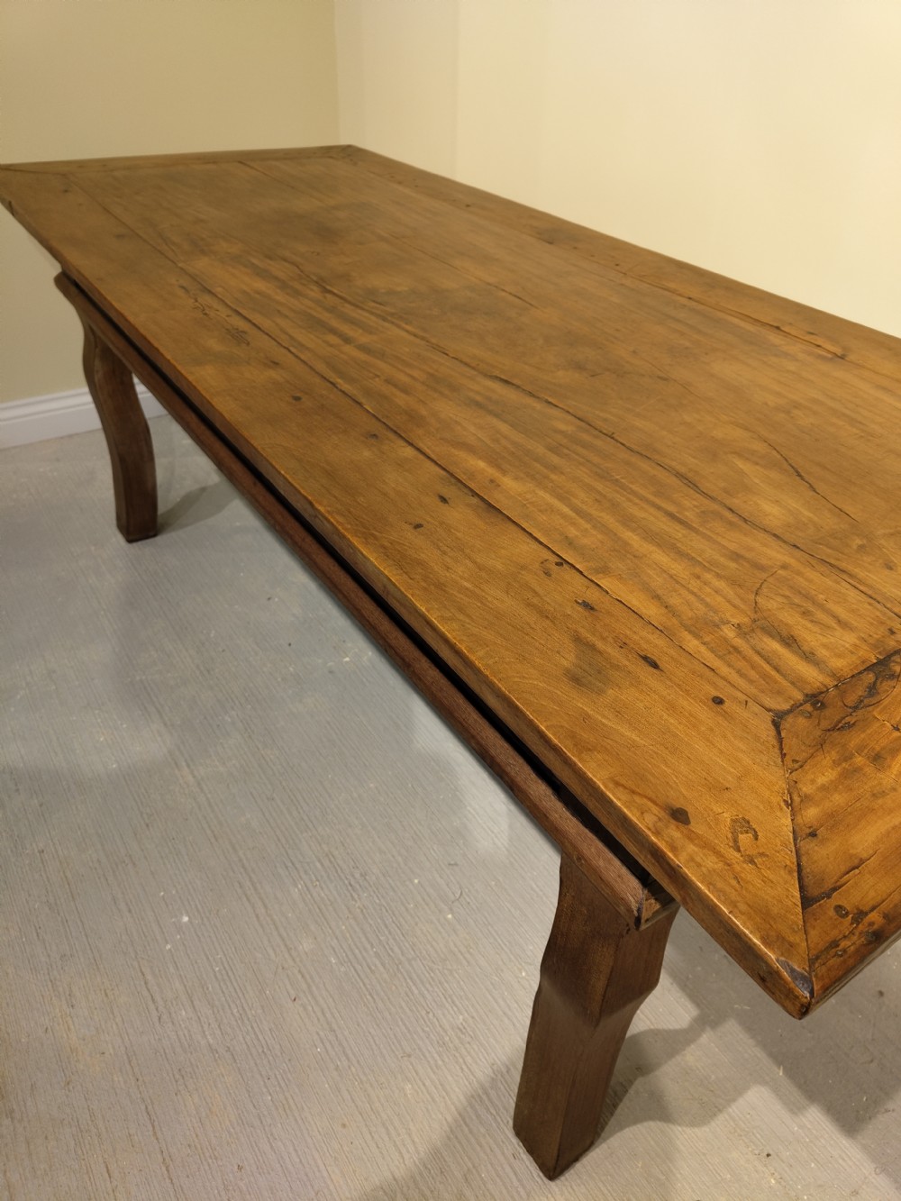 A long rectangular antique fruitwood farmhouse dining table featuring a planked top and subtly curved legs.