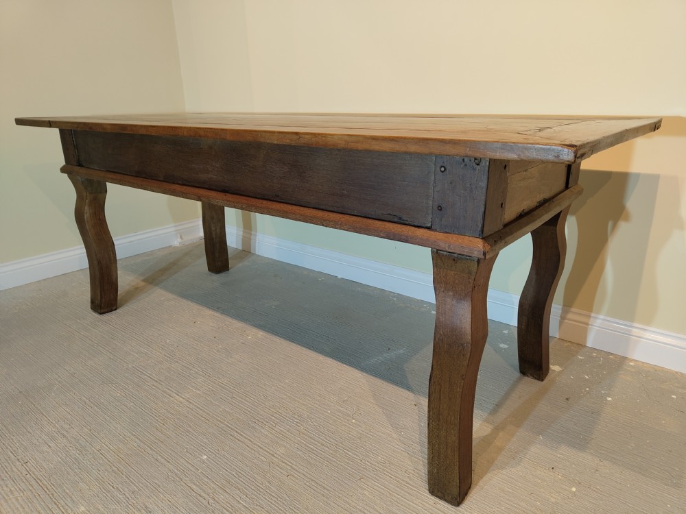 A long rectangular antique fruitwood farmhouse dining table featuring a planked top and subtly curved legs. View III