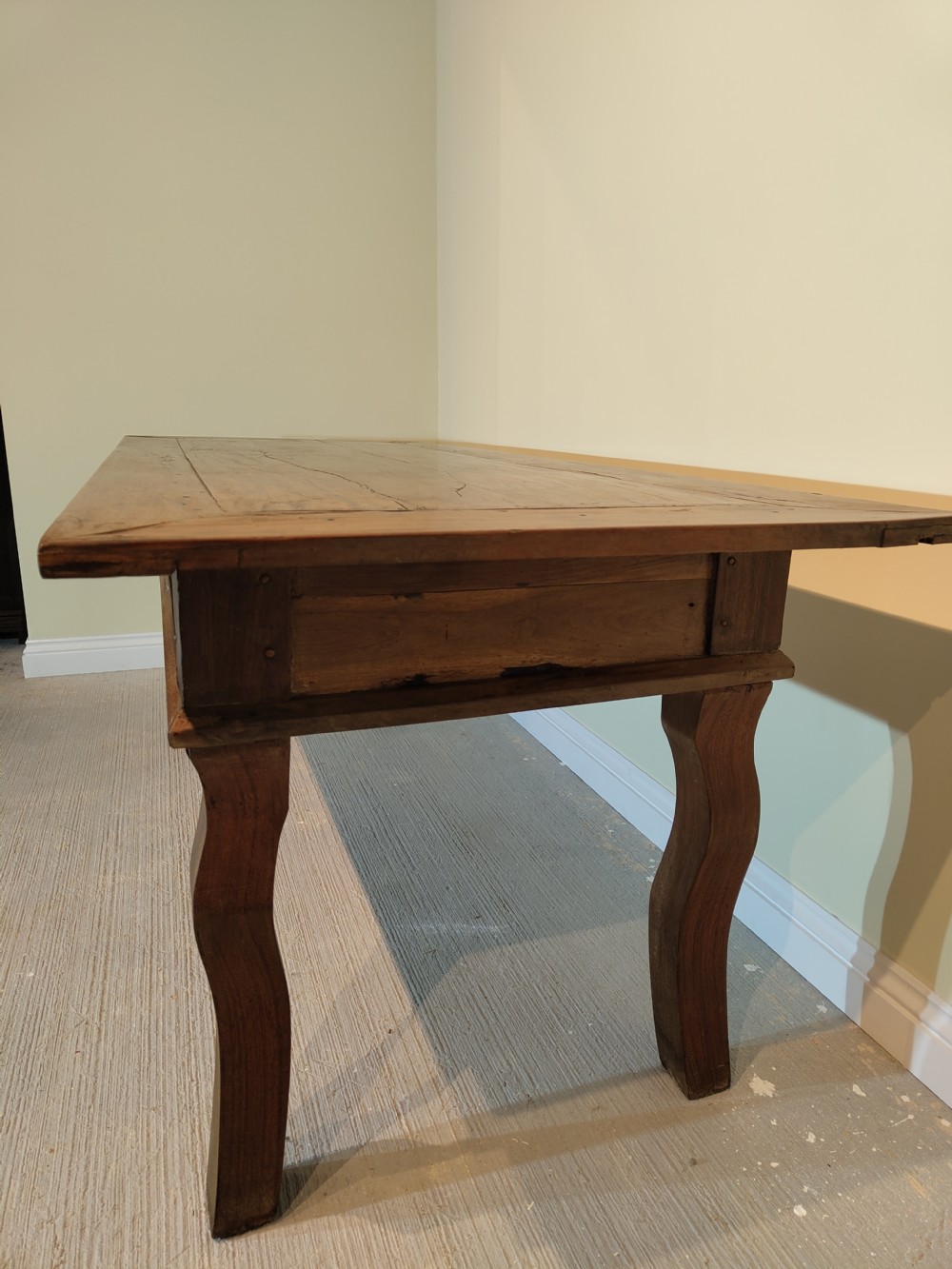 A long rectangular antique fruitwood farmhouse dining table featuring a planked top and subtly curved legs. View V