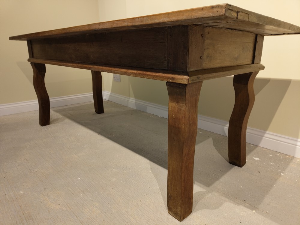 A long rectangular antique fruitwood farmhouse dining table featuring a planked top and subtly curved legs. View VI
