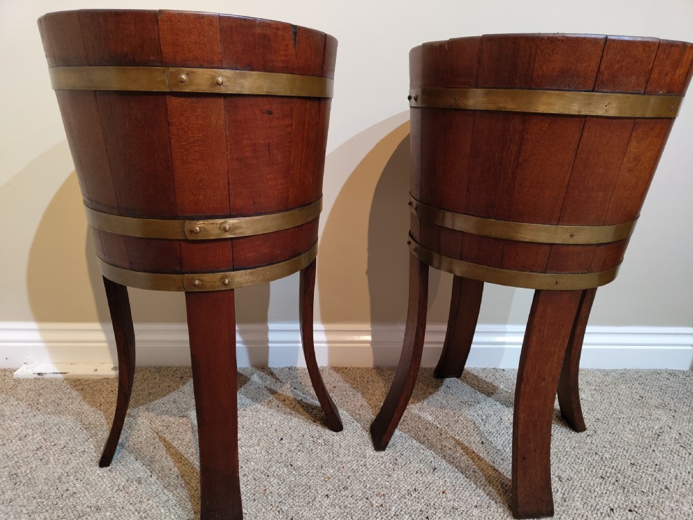 A pair of antique mahogany coopered bucket jardinieres with polished brass straps standing on splayed wooden legs. View III