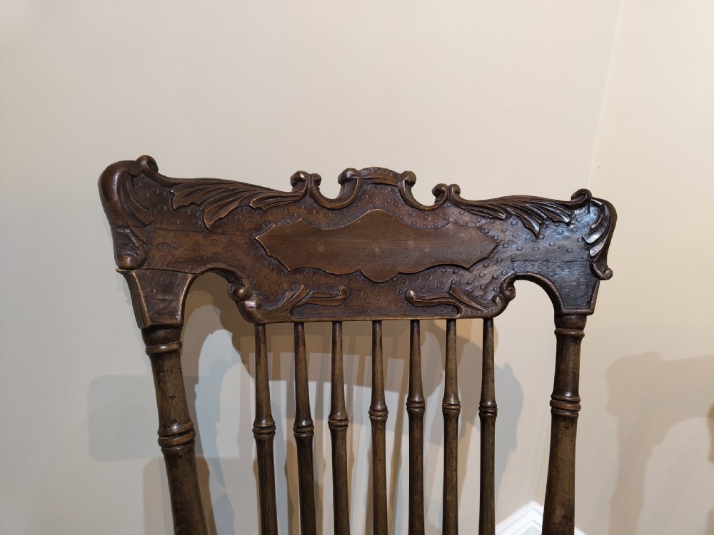 A pair of matching dark brown wooden rocking chairs featuring carved crest rails, spindle backrests, shaped wooden seats, and turned legs on curved runners. View IV