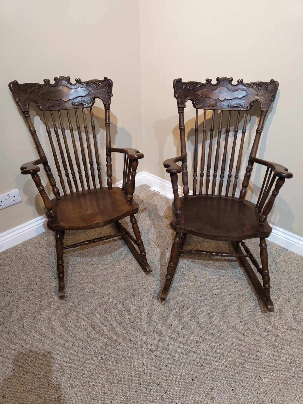 A pair of matching dark brown wooden rocking chairs featuring carved crest rails, spindle backrests, shaped wooden seats, and turned legs on curved runners.