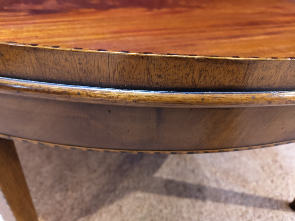 An oval mahogany coffee table with a raised tray edge detail, flame mahogany top veneer, and four square tapered legs. View IV