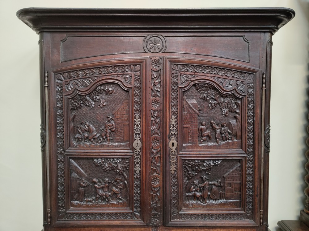 An antique dark oak French Provincial dresser featuring intricate relief carvings of figurative village scenes on four cupboard doors and three drawers. View III