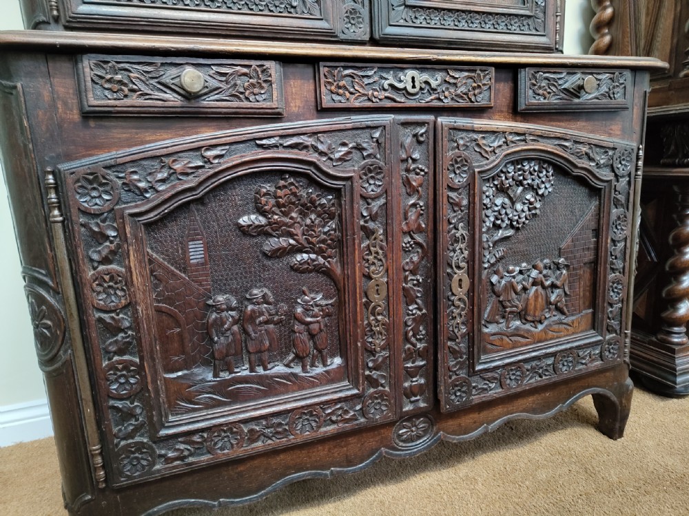 An antique dark oak French Provincial dresser featuring intricate relief carvings of figurative village scenes on four cupboard doors and three drawers. View IV