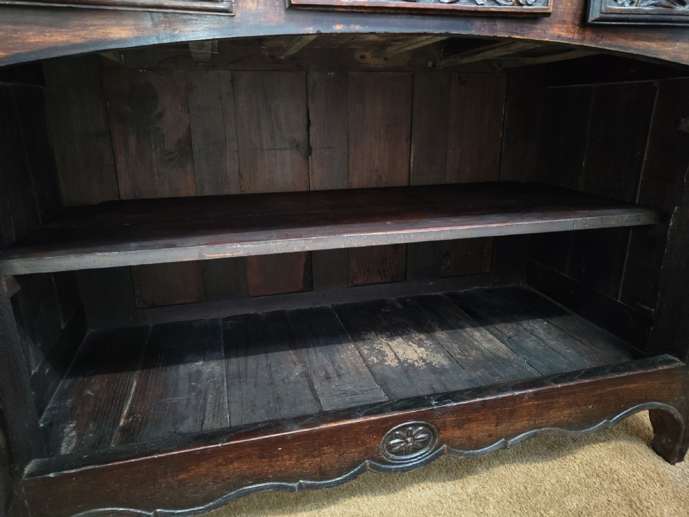 An antique dark oak French Provincial dresser featuring intricate relief carvings of figurative village scenes on four cupboard doors and three drawers. View XII