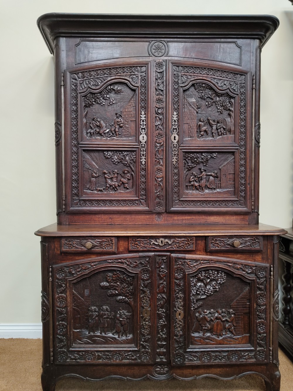 An antique dark oak French Provincial dresser featuring intricate relief carvings of figurative village scenes on four cupboard doors and three drawers.
