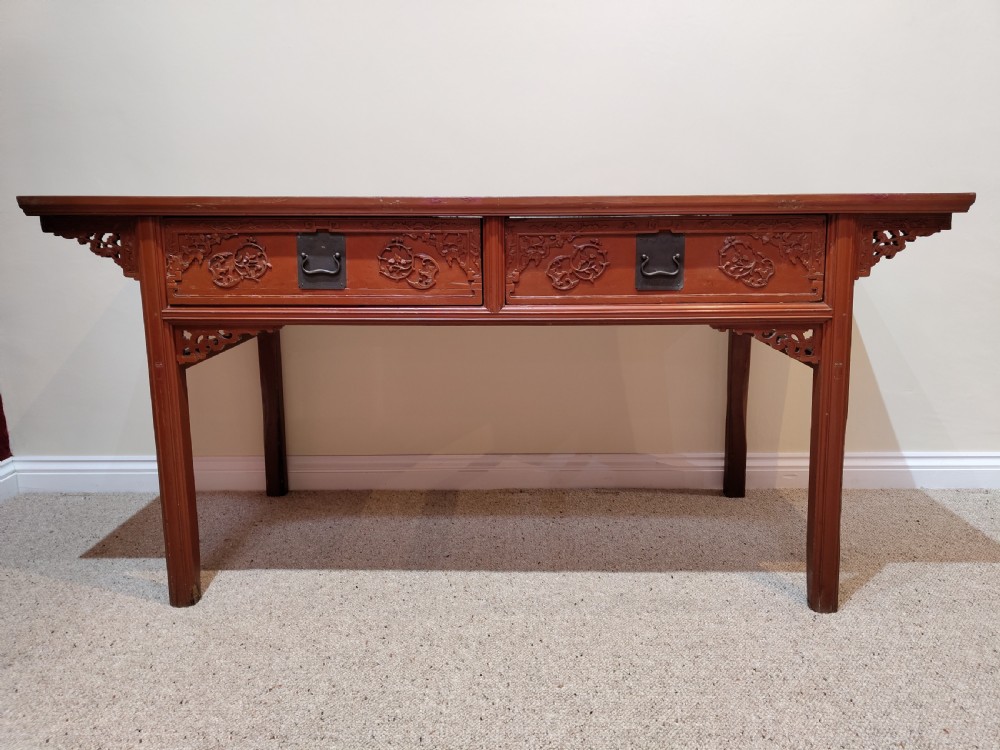 An antique Chinese red lacquer console table featuring two carved drawers with dark metal handles and extended top edges.
