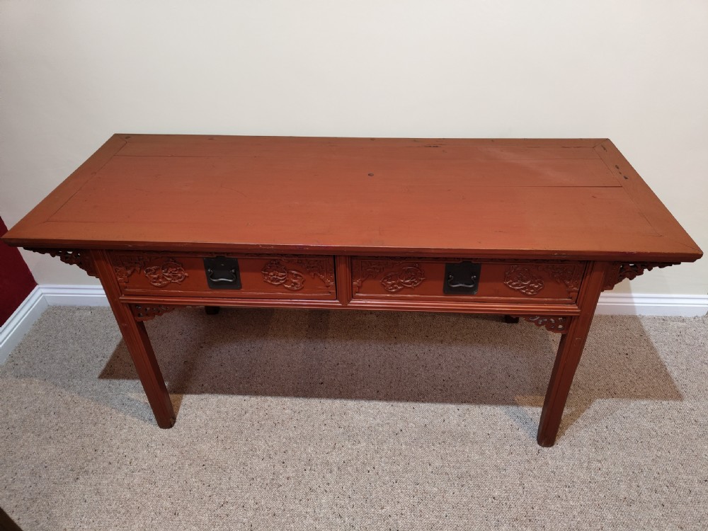 An antique Chinese red lacquer console table featuring two carved drawers with dark metal handles and extended top edges. View III