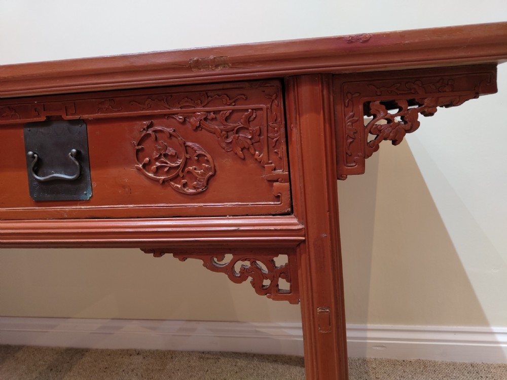 An antique Chinese red lacquer console table featuring two carved drawers with dark metal handles and extended top edges. View IV