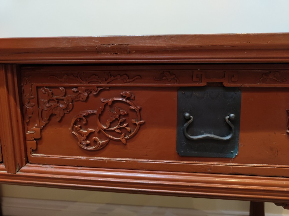 An antique Chinese red lacquer console table featuring two carved drawers with dark metal handles and extended top edges. View VII