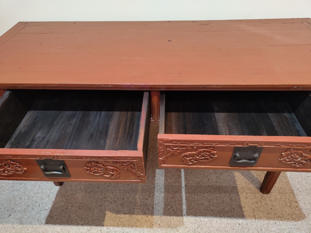 An antique Chinese red lacquer console table featuring two carved drawers with dark metal handles and extended top edges. View VIII