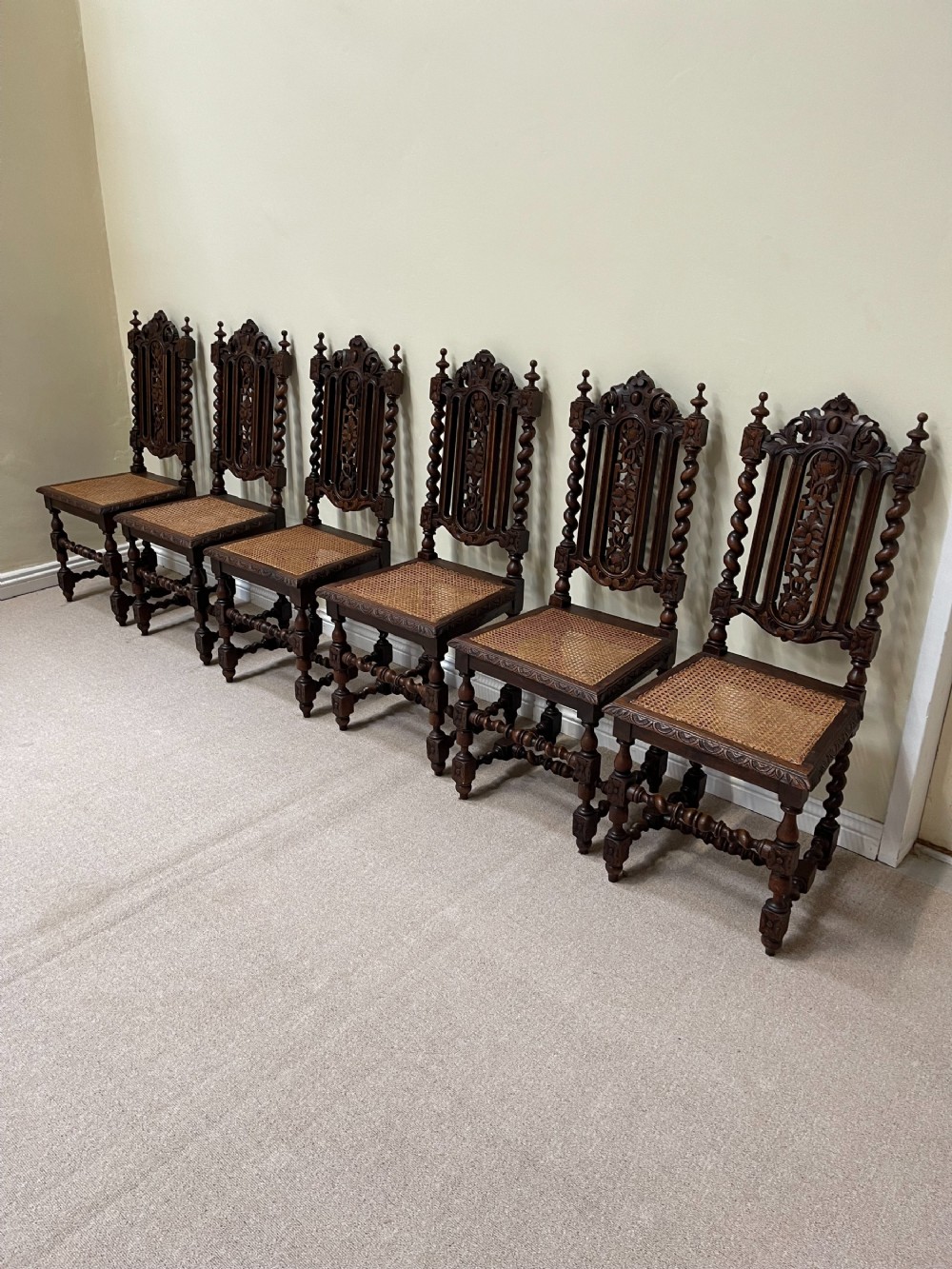 A set of six dark carved oak dining chairs featuring barley twist uprights, ornate backrests, and woven cane seats.