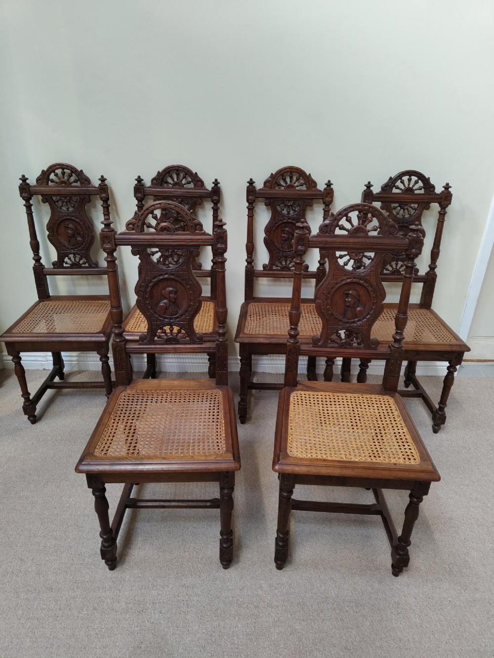 A set of six dark oak Breton dining chairs featuring carved portrait splats, ship wheel crests, and woven cane seats.