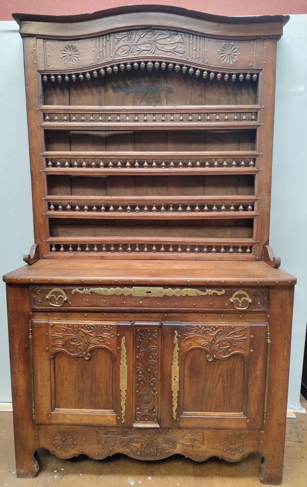 An antique warm brown carved oak French provincial dresser featuring an upper open plate display rack with turned spindles above a two-door base cupboard with brass fitments.