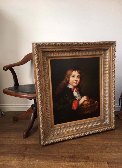 fig 2. A framed portrait of a young boy with reddish-brown hair holding a basket of fruit, set within an ornate gilded frame.