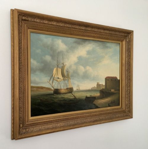 fig 3. A 19th-century style marine oil painting on panel depicting a large sailing warship anchored near a stone coastal fortification under a cloudy sky, presented in a heavily moulded gold gilt frame.