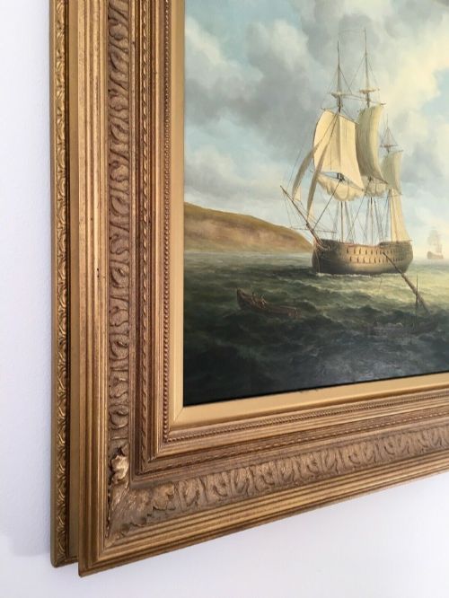 fig 6. A 19th-century style marine oil painting on panel depicting a large sailing warship anchored near a stone coastal fortification under a cloudy sky, presented in a heavily moulded gold gilt frame.