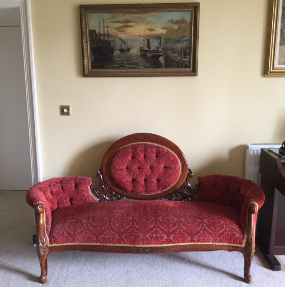A Victorian-style carved mahogany settee featuring a tufted oval central backrest and buttoned scrolled arms upholstered in burgundy brocade fabric.