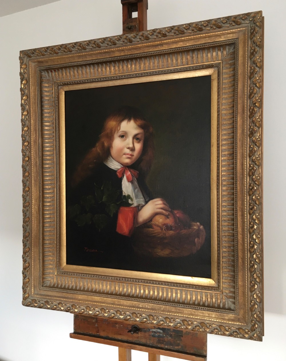 A framed portrait painting of a young boy holding a fruit basket, presented inside a carved gilded wood frame. View V