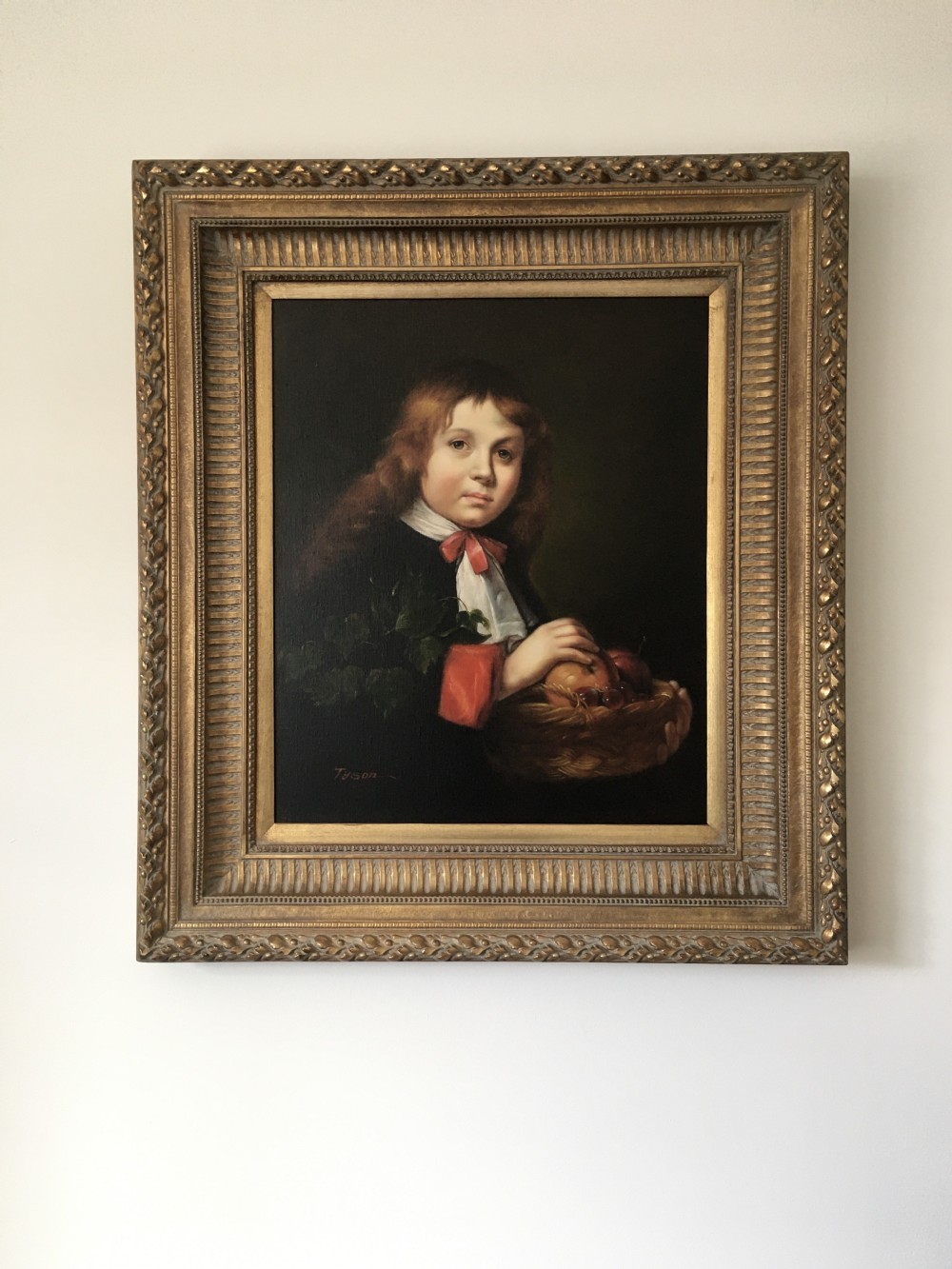A framed portrait painting of a young boy holding a fruit basket, presented inside a carved gilded wood frame. View IV