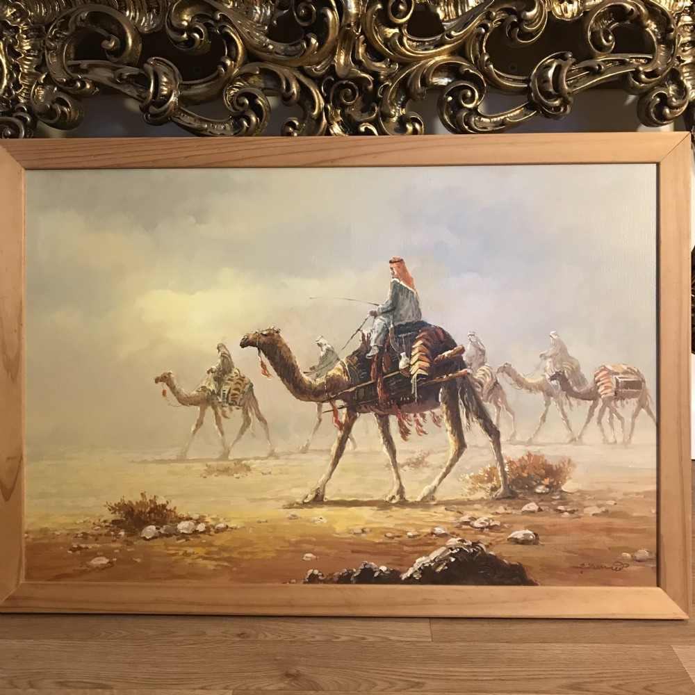 An oil painting on canvas depicting a Bedouin camel caravan traversing a desert landscape under a hazy sky, encased in a simple light wood frame. View XIV