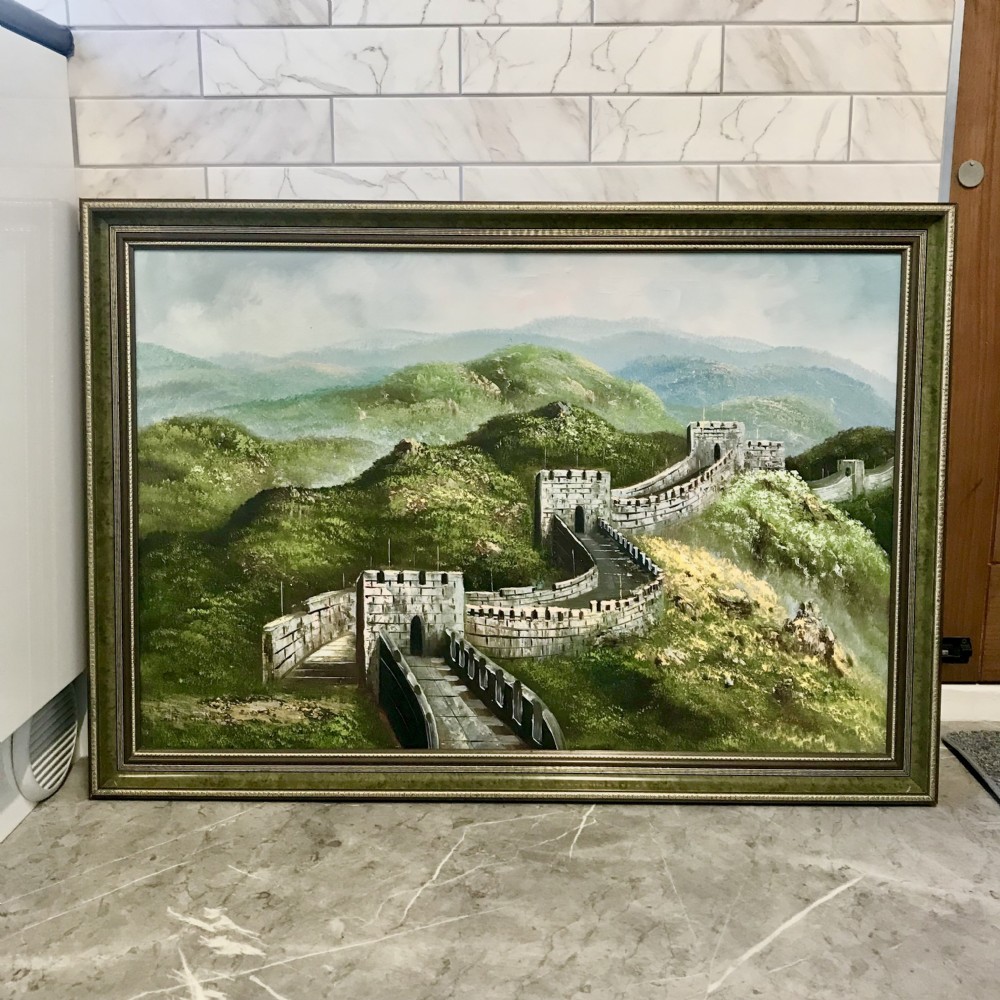 A large horizontal oil painting depicting the Great Wall of China winding through lush green mountains under a cloudy sky, encased in a metallic green and gold frame. View XVIII