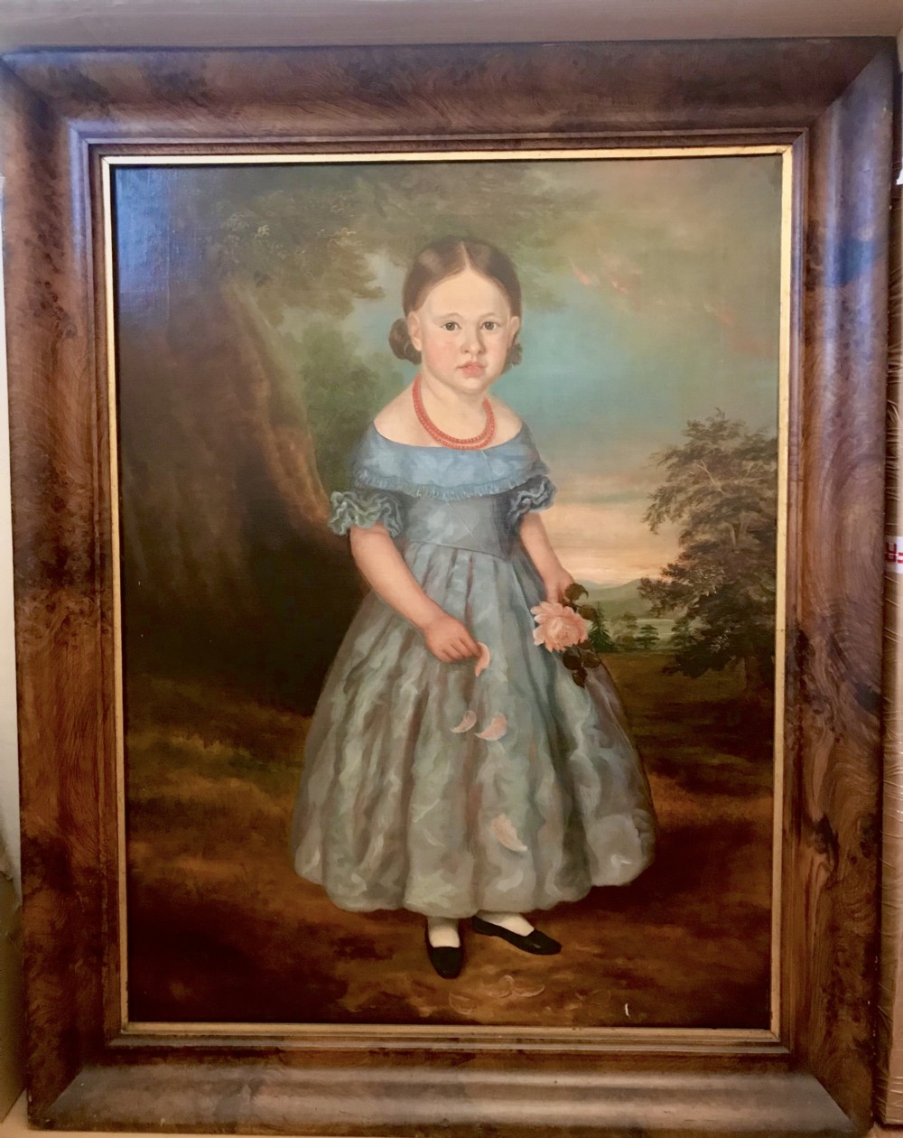 An antique oil painting depicting a standing young girl in a blue dress holding a rose, set within a wide timber frame with a gilded inner rim. View XIII