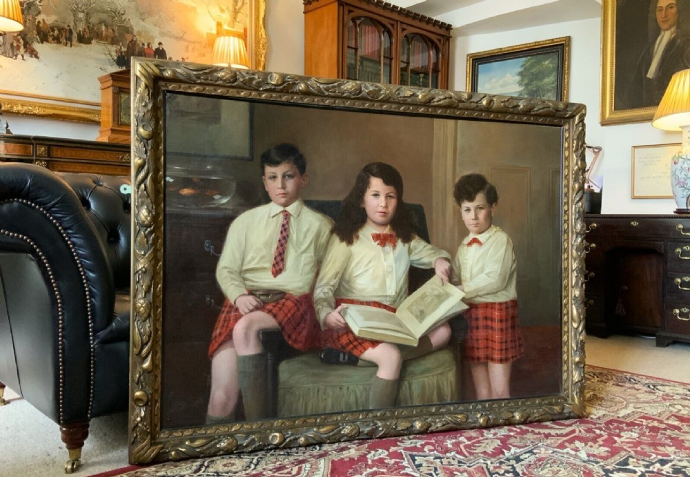 A large framed oil painting depicting three children seated together wearing red tartan kilts within a carved gilded frame. View XV