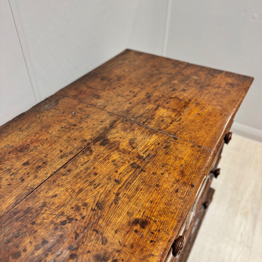 A seventeenth-century dark oak chest featuring three drawers decorated with geometric panel mouldings, wooden turned handles, brass escutcheons, and bun feet. View VI
