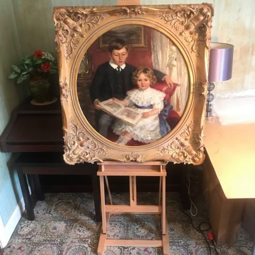 An Edwardian oil portrait painting depicting a young boy and girl reading a book together, presented within a square gilt frame featuring an oval aperture. View III